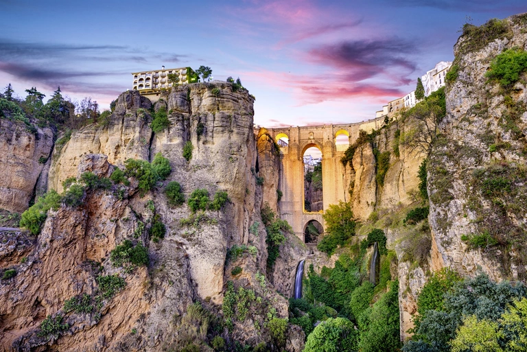 Puente Nuevo in Ronda bei Sonnenuntergang Die Puente-Nuevo-Brücke überspannt eine tiefe Schlucht in Ronda, Spanien, mit historischen Gebäuden auf den Felsen bei Sonnenuntergang.