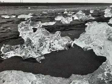 Klare Eisstücke liegen verstreut auf dem schwarzen Lavastrand von Diamond Beach in Island. Das faszinierende Zusammenspiel aus Eis, Meer und dunklem Sand zeigt die einzigartige Naturkulisse des Nordens und macht Island zue