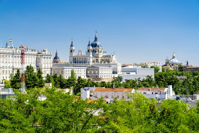 Königspalast und Almudena-Kathedrale in Madrid Stadtansicht von Madrid mit dem Königspalast und der Almudena-Kathedrale über grünen Baumkronen bei klarem Himmel