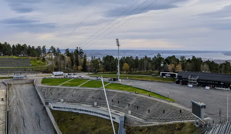 Die beeindruckende Holmenkollen-Skisprungschanze in Oslo, Norwegen, mit Blick über die Zuschauertribünen auf die Stadt und den Fjord im Hintergrund – eine faszinierende Sehenswürdigkeit für eine unvergessliche Reise.