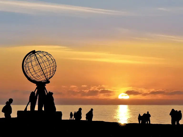 Nordkap Norwegen – Magischer Sonnenuntergang am nördlichsten Punkt Europas Besucher stehen am Nordkap vor der markanten Globus-Skulptur und beobachten den Sonnenuntergang über dem Nordmeer. Das goldene Licht und die Silhouetten vermitteln die einzigartige Stimmung einer Reise zum äußersten Norden Europas.