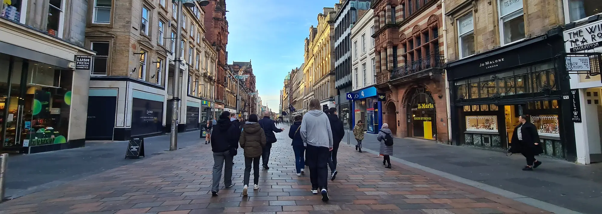 Städtetrip Glasgow: Pulsierendes Leben auf der Einkaufsmeile Buchanan Street Menschen spazieren an einem sonnigen Tag über die belebte Einkaufsmeile Buchanan Street in Glasgow, Schottland, deren historische Architektur zahlreiche Geschäfte beherbergt und das pulsierende Flair eines unvergesslichen Städtetrips auf einer Reise vermittelt.
