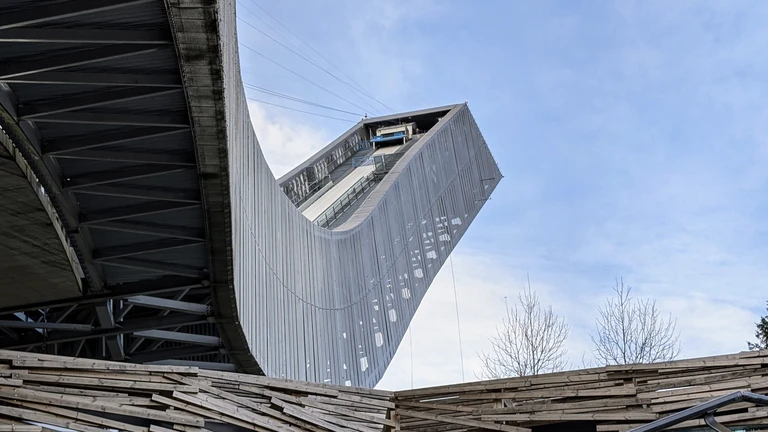 Auf diesem Bild ist die beeindruckende Skisprungschanze auf dem Holmenkollen in Oslo aus einer dramatischen Froschperspektive zu sehen. Die Aufnahme unterstreicht die moderne, geschwungene Architektur der Anlage, die sich als eines der Wahrzeichen der Stadt in den Himmel erstreckt.
