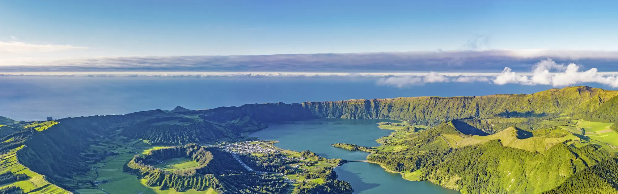 Sete Cidades auf São Miguel – Kraterlandschaft und Vulkansee der Azoren mit Wolters Rundreisen entdecken „Panoramablick auf die beeindruckende Vulkanlandschaft Sete Cidades auf São Miguel, Azoren. Grüne Berghänge umrahmen den blaugrünen Kratersee, während im Hintergrund der Atlantik und eine Wolkenlinie am Horizont zu sehen sind – eine der bekanntesten Natursehenswürdigkeiten Portugals.