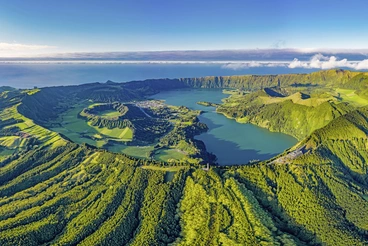 Luftaufnahme der Kraterlandschaft von Sete Cidades auf São Miguel, Azoren: Zwei große Vulkanseen liegen eingebettet in einen grünen Krater, umgeben von sanften Hügeln und üppiger Vegetation unter blauem Himmel.