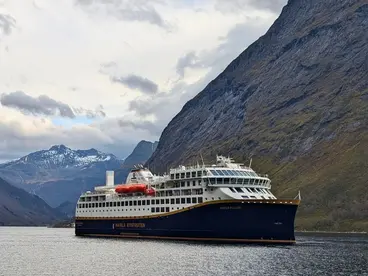 Das Postschiff Havila fährt auf einer Postschiffreise durch die beeindruckenden norwegischen Fjorde – umgeben von majestätischen Bergen und schneebedeckten Gipfeln.