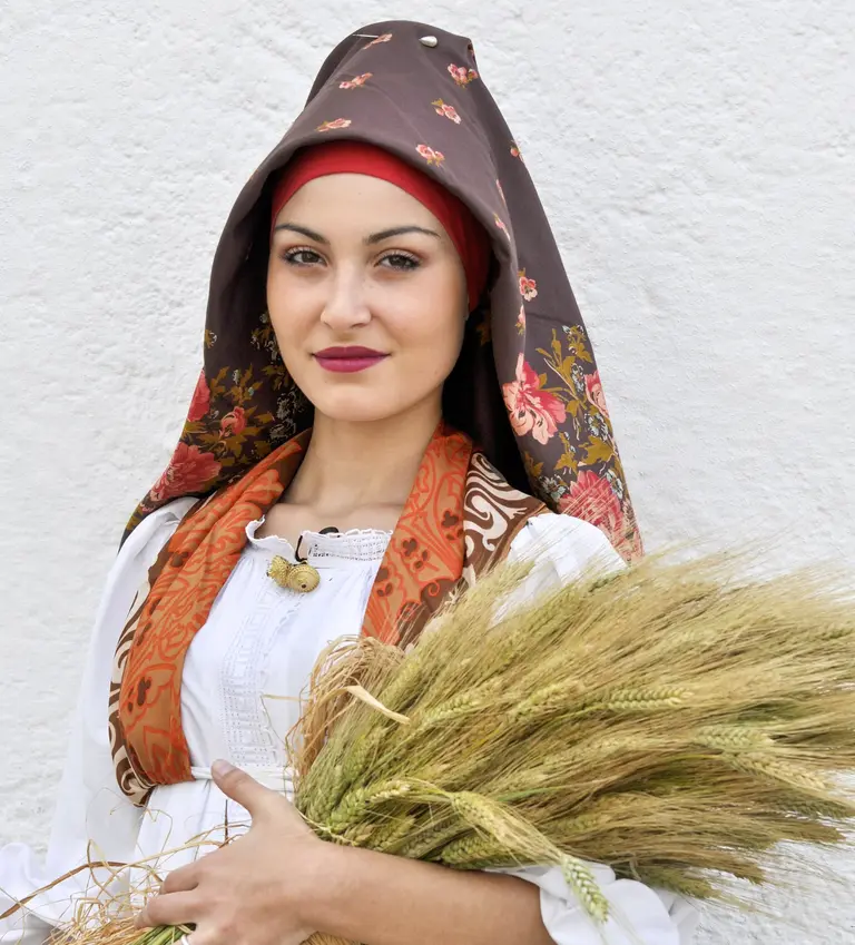 Porträt einer Frau in traditioneller sardischer Tracht mit buntem Kopftuch und Getreidebündel – Darstellung italienischer Kultur und Tradition.