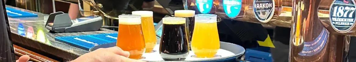 Bier-Tasting in Tromsø Auf diesem Bild ist ein Tablett mit verschiedenen Biersorten für eine Bierprobe (Tasting Flight) in der Mack-Brauerei in Tromsø zu sehen. Im Hintergrund erkennt man die Zapfhähne der Brauerei, die als die nördlichste der Welt bekannt ist und eine beliebte Anlaufstelle für Bierliebhaber darstellt.