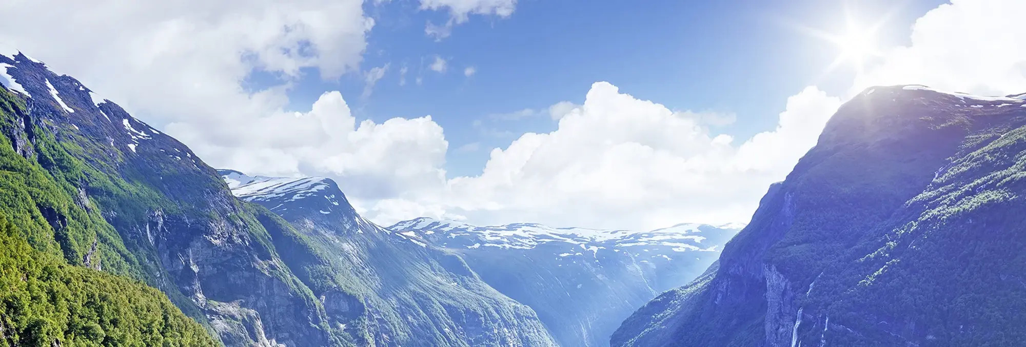 Atemberaubender Blick auf den Geirangerfjord in Norwegen - UNESCO Weltnaturerbe und Wasserfall-Panorama Panoramablick auf den Geirangerfjord in Norwegen mit steilen, grünen Bergen und einem Wasserfall, der senkrecht in das ruhige Fjordwasser stürzt. UNESCO-Weltnaturerbe, bekannt für seine dramatische Landschaft und klare Luft.