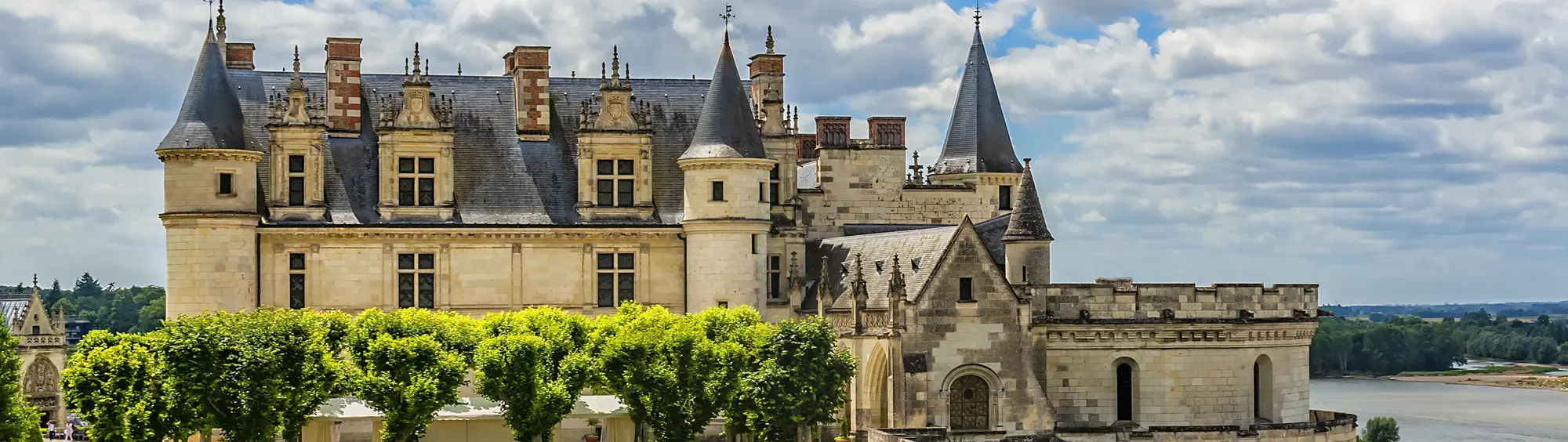 Das Schloss Amboise an der Loire in Frankreich mit seinen markanten Türmen und der weitläufigen Schlossanlage. Im Vordergrund der gepflegte Schlossgarten, im Hintergrund der Fluss Loire mit der historischen Steinbrücke sowie der malerischen Landschaft des Loire-Tals. Beliebtes Reiseziel für Kultur- und Frankreichreisen.
