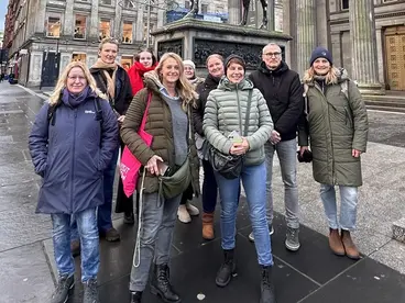 Eine Gruppe von Reiseteilnehmenden steht vor einer Reiterstatue im Stadtzentrum von Glasgow in Schottland. Im Hintergrund sind historische Gebäude und Denkmäler zu sehen. Das Bild zeigt einen FAM Trip und gemeinsame Erlebnisse bei einer Gruppenreise in Europa.