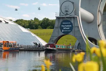 Falkirk Wheel: Schottlands einzigartiges Schiffshebewerk erleben Das beeindruckende Schiffshebewerk Falkirk Wheel in Schottland, wo an einem sonnigen Tag Ausflugsboote im Wasserbecken liegen und diese technische Meisterleistung als einzigartige Sehenswürdigkeit zu einer unvergesslichen Reise und einem erlebnisreichen Urlaub einlädt.