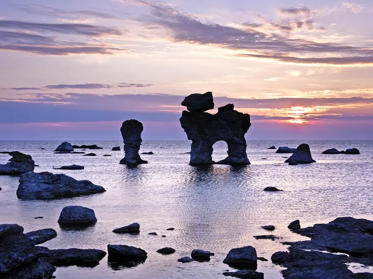 Spektakuläre Felsformationen, sogenannte Raukar, ragen vor der Küste der schwedischen Insel Gotland aus dem Meer. Im goldvioletten Licht des Sonnenuntergangs spiegeln sich die bizarren Kalksteinfiguren im ruhigen Wasser der Ostsee. Eine eindrucksvolle Naturlandschaft, die Gotland zu einem besonderen Reiseziel in Schweden macht.
