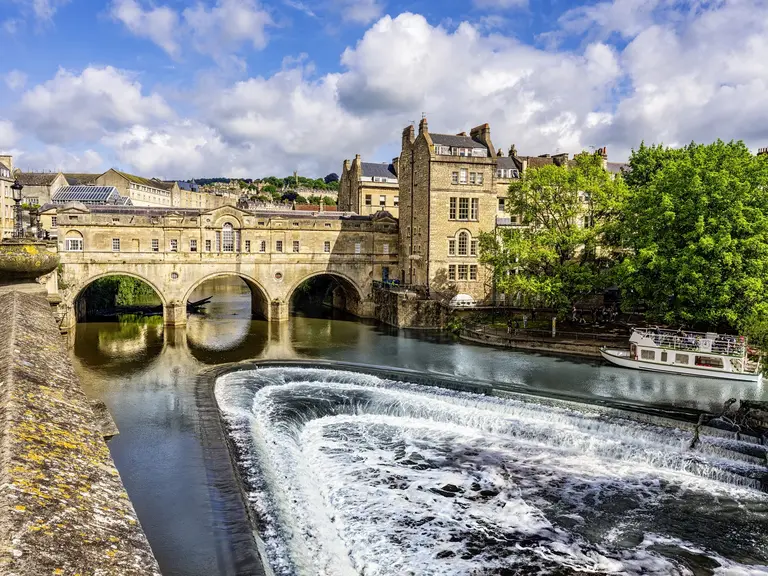 Die berühmte Pulteney Bridge in Bath mit Geschäften auf beiden Seiten und Blick auf den Fluss Avon mit Kaskaden.