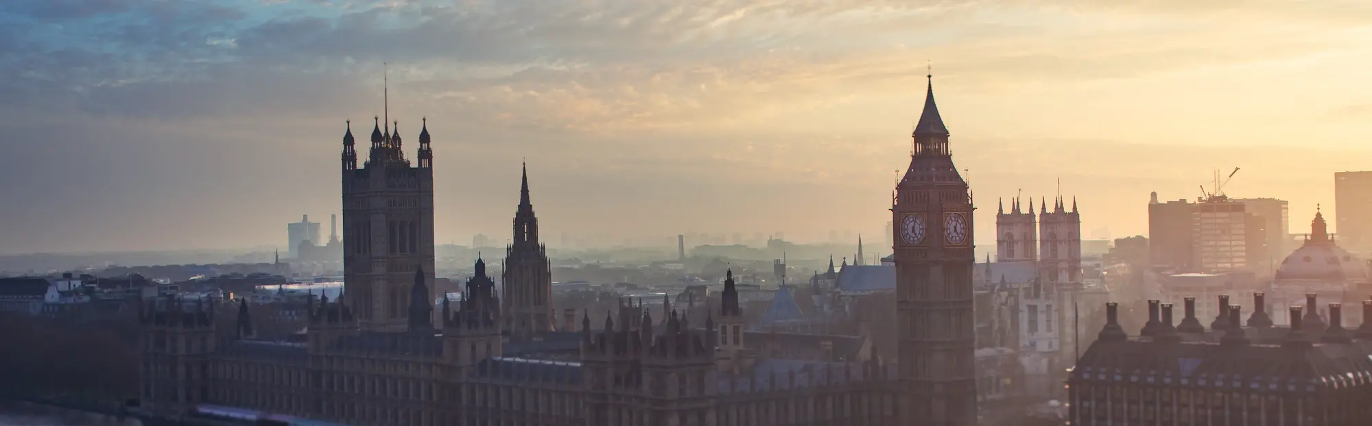 Panorama von London mit Big Ben und den Houses of Parliament in warmem Abendlicht und leichtem Nebel.
