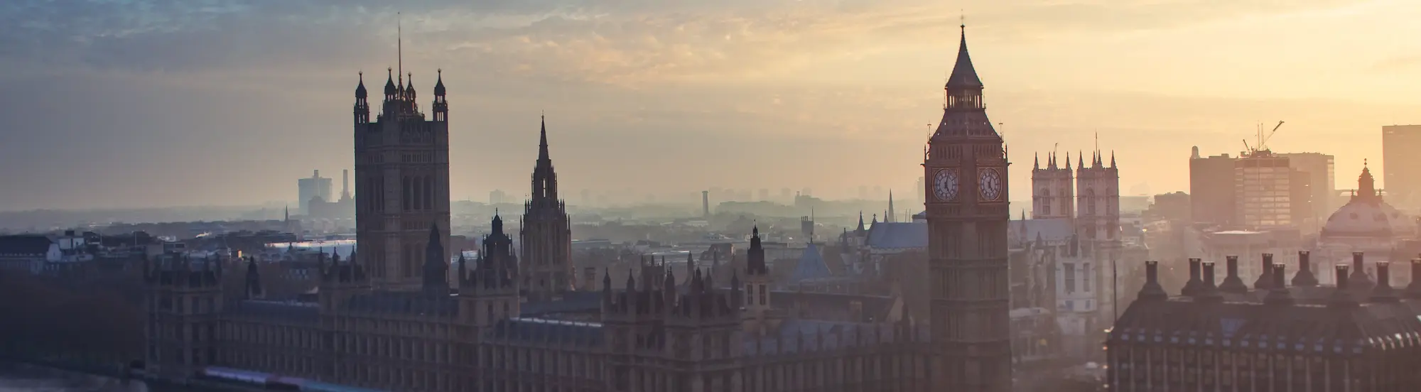 Panorama von London mit Big Ben und den Houses of Parliament in warmem Abendlicht und leichtem Nebel.