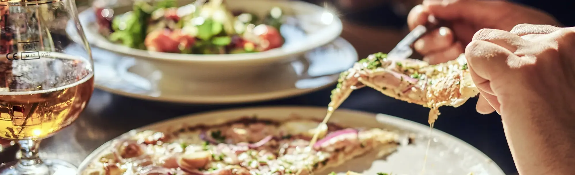 Nahaufnahme von italienischer Pizza mit geschmolzenem Käse, einem Glas Bier und frischem Salat – typische kulinarische Genüsse in Italien.