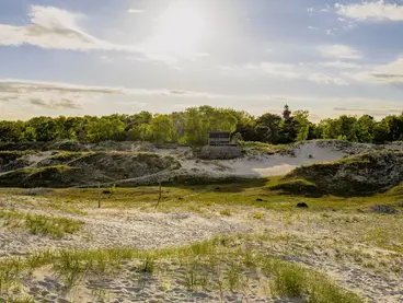 eine Landschaft mit kleinen Hügeln welche teils mit Sand und teils mit Gras bedeckt sind.