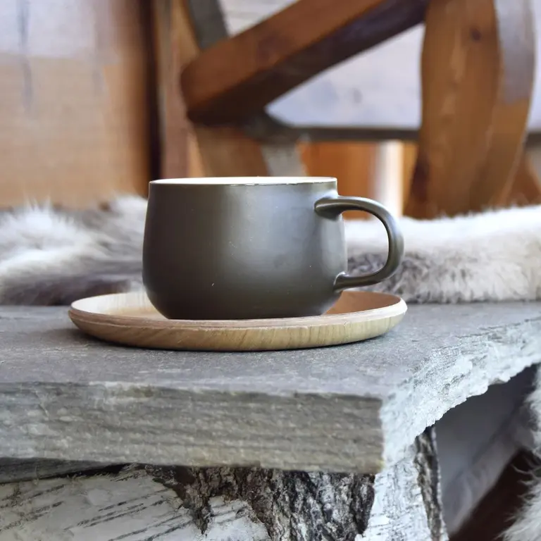 Schwarze Tasse mit Espresso auf einem Holzuntersetzer, serviert auf einer rustikalen Steinplatte - typisch italienische Kaffeekultur. 