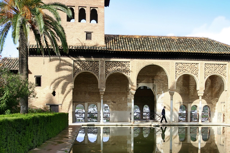 Eine elegante Arkade der Alhambra spiegelt sich in einem klaren Wasserbecken, umgeben von Palmen und Gärten. Der maurische Baustil und die ruhige Atmosphäre verkörpern die kulturelle Vielfalt Andalusiens. Dieses Motiv zeigt die Verbindung von Architektur, Natur und Geschichte, die Granada zu einem faszinierenden Reiseziel macht.