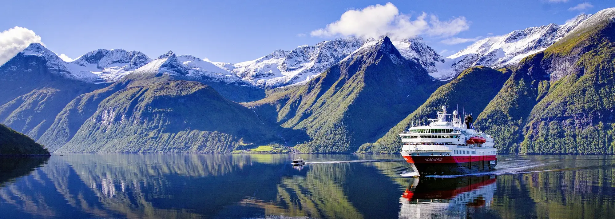 Hurtigruten Schiff gleitet über norwegischen Fjord im Hintergrund sind schöne Berge zu sehen, bei strahlendem Wetter