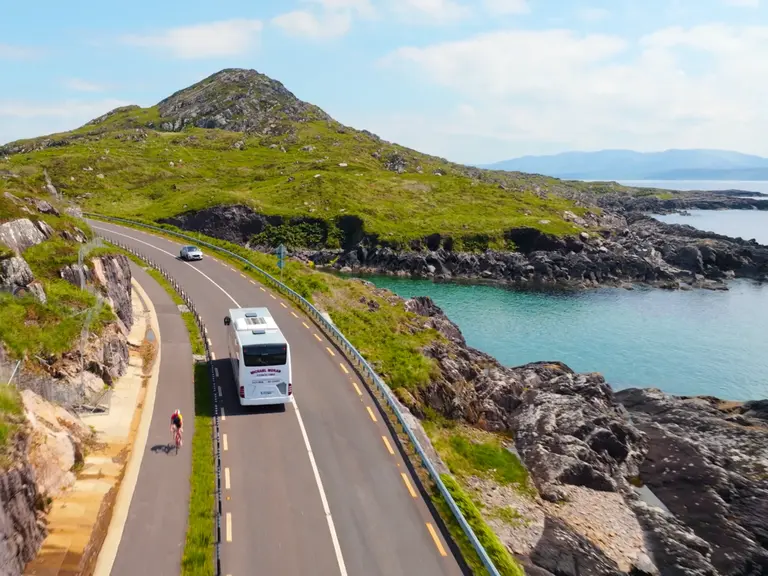 Autofahren auf dem Ring of Kerry Auto und Reisebus auf der Küstenstraße des Ring of Kerry in Irland – beliebte Panoramaroute mit Meerblick und grünen Hügeln.