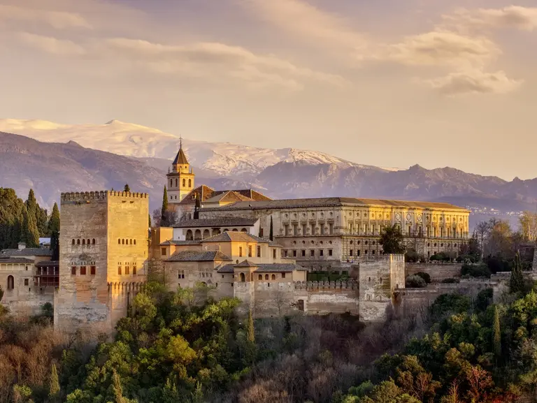 Die Alhambra in Granada erstrahlt im warmen Abendlicht vor der Kulisse der schneebedeckten Sierra Nevada. Die beeindruckende Festungsanlage mit ihren filigranen Türmen und Mauern zählt zu den bedeutendsten Sehenswürdigkeiten Andalusiens und ist ein Symbol für Spaniens maurische Geschichte und architektonische Schönheit.