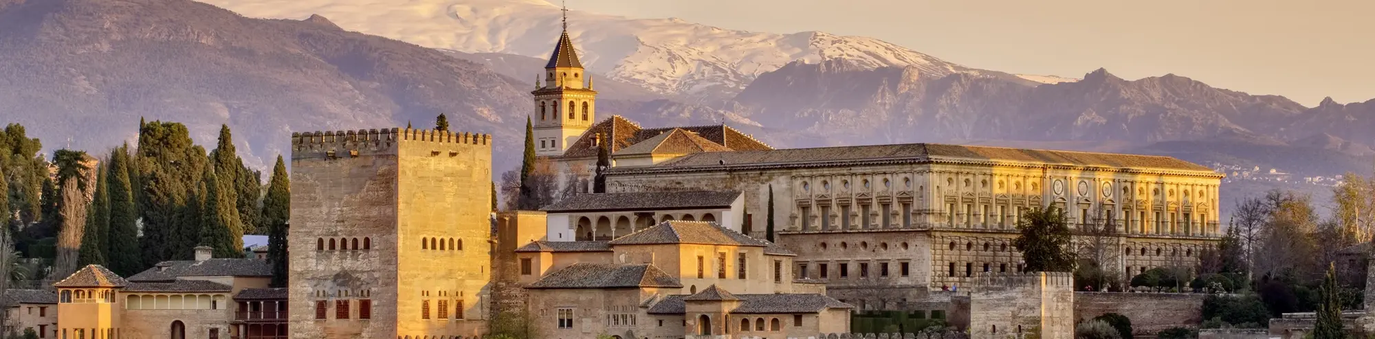Die Alhambra in Granada erhebt sich im warmen Abendlicht vor der schneebedeckten Sierra Nevada. Das historische Bauwerk mit seinen Palästen und Gärten ist ein Wahrzeichen Andalusiens und gehört zum UNESCO-Welterbe. Das Bild fängt die Magie des Sonnenuntergangs über der maurischen Architektur ein - ein Highlight jeder Spanienreise.