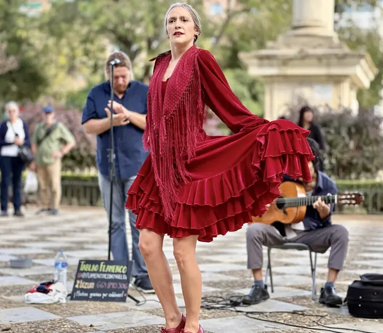 Eine Flamenco-Tänzerin in rotem Kleid wirbelt mit ausdrucksstarker Bewegung zu Gitarrenmusik auf einem Platz in Granada. Das Bild vermittelt die Emotion und Energie des traditionellen andalusischen Tanzes und steht für Spaniens kulturelle Seele - ein unvergessliches Erlebnis für alle, die Musik, Leidenschaft und Reisen verbinden möchten.