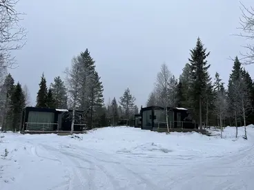Design-Glas-Villa in Lappland: Einzigartige Übernachtung mit Panoramablick Das luxuriöse Interieur einer modernen Glas-Villa in Lappland, wo ein gemütliches Bett direkt vor einem riesigen Panoramafenster mit Blick auf die verschneite Natur steht und das Glasdach eine unvergessliche Übernachtung während eines Winter-Urlaubs verspricht, ideal für das Abenteuer der Nordlichter-Beobachtung.