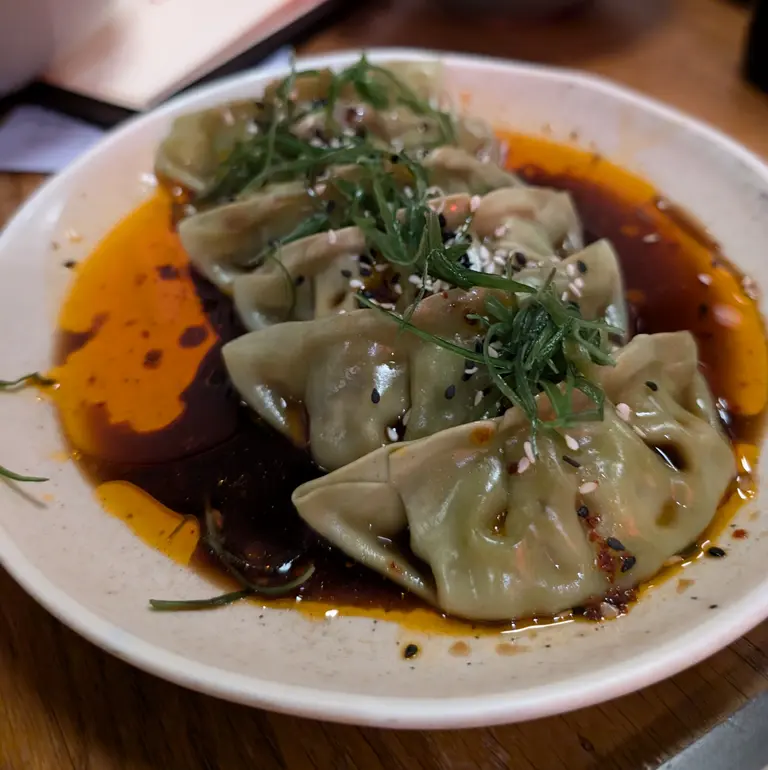 Appetitlich angerichtet sind hier asiatische Teigtaschen, die in einer Sauce aus Chili-Öl schwimmen. Garniert mit frischen Frühlingszwiebeln und Sesam, verspricht diese in einem Restaurant servierte Vorspeise ein würziges und aromatisches Geschmackserlebnis.