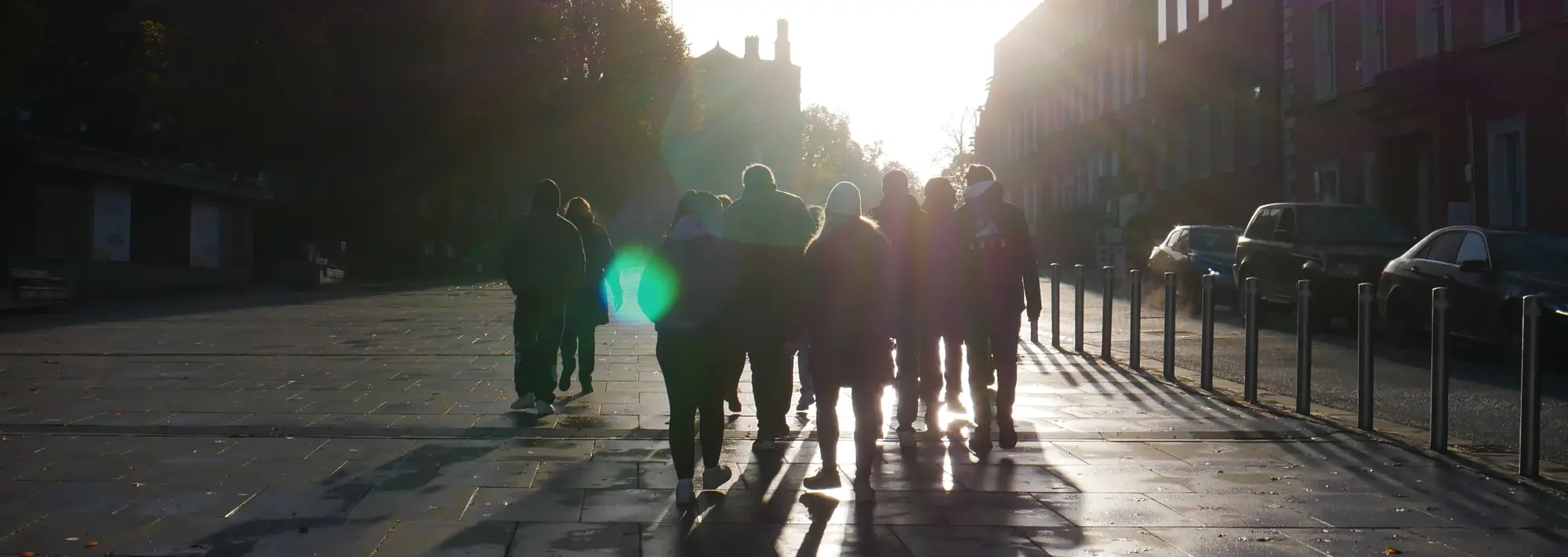 Azubis unterwegs in Irland im schimmernden Licht Gegen die tiefstehende Sonne läuft hier eine Gruppe von Menschen über einen städtischen Platz. Die Aufnahme fängt eine alltägliche Szene ein, die durch das starke Gegenlicht und die langen Schatten eine besondere, fast malerische Atmosphäre erhält.