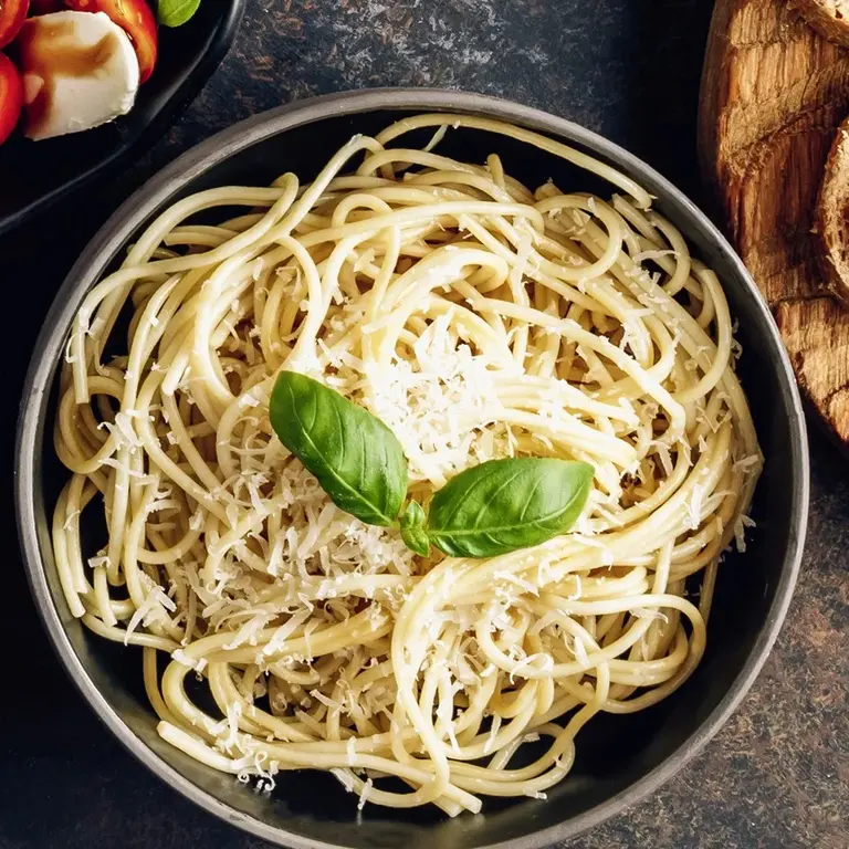 Teller mit Spaghetti, Knoblauch, Olivenöl und frisch geriebenem Parmesan – einfache und beliebte italienische Pasta-Spezialität.