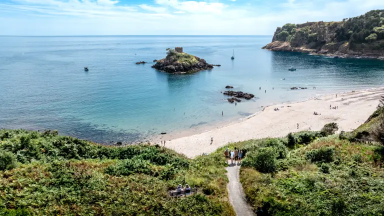 Portelet Bay Zu sehen ist ein riesigere Badestrand und Wasser welches sich Kilometerweit erstreckt. Viele Menschen sind hier zu sehen.