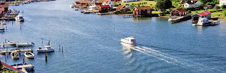 Boot fährt durch einen Schärenkanal bei Bohuslän, umgeben von kleinen Inseln und typischen roten Holzhäusern. Sommerliches Küstenpanorama in Westschweden.